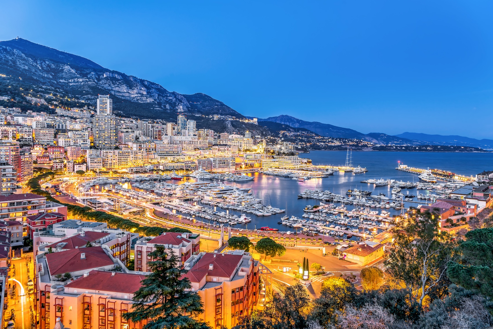 Panoramic aerial view of Monaco Port Hercule at night with luxury yachts and illuminated cityscape, prime location for Monaco real estate