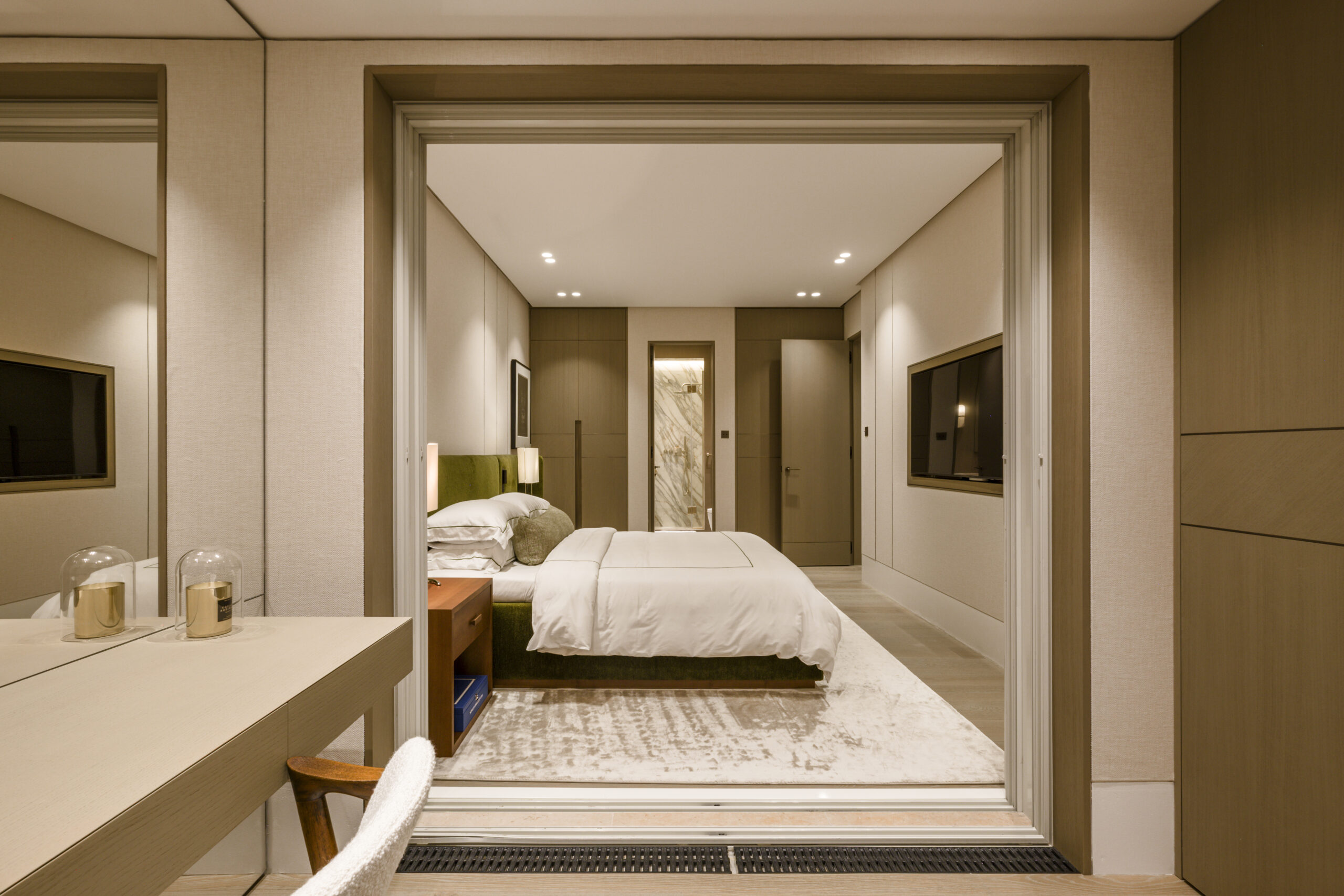 View from the dressing area into the master bedroom of a Seaside Plaza apartment in Monaco with green upholstered bed, wall panelling and en suite bathroom beyond